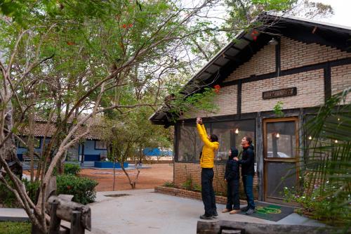 two people standing in front of a house with a man reaching for a tree at Pousada Rio Claro in Poconé