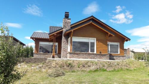 una casa de madera con chimenea de ladrillo y ventanas en Mi casita en la loma en Trevelín