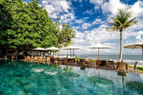 a swimming pool with chairs and umbrellas and the ocean at Bali Garden Beach Resort in Kuta