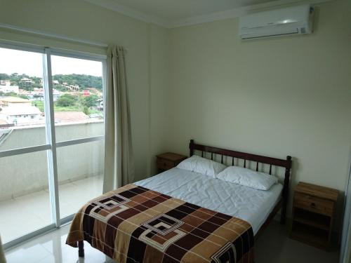 1 dormitorio con cama y ventana grande en Apto no centro de Bombinhas, en Bombinhas
