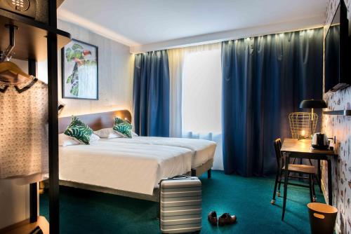 a bedroom with a bed with blue curtains and a table at KOPSTER Hotel Lyon Groupama Stadium in Décines-Charpieu
