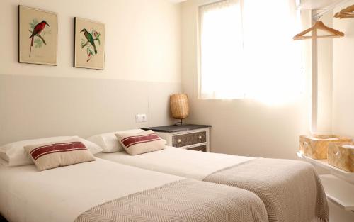 a white bedroom with two beds and a window at Apartamentos Plaza Mayor in Gijón