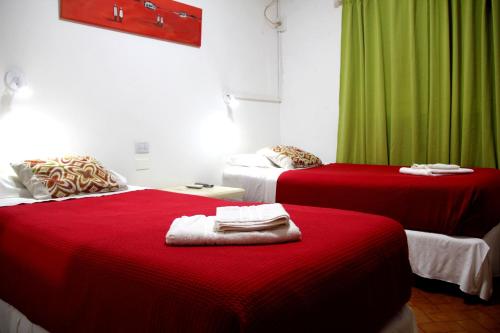 two beds with red sheets in a room with green curtains at Hotel Vuelta del Ombu in Gobernador Ingeniero Valentín Virasoro