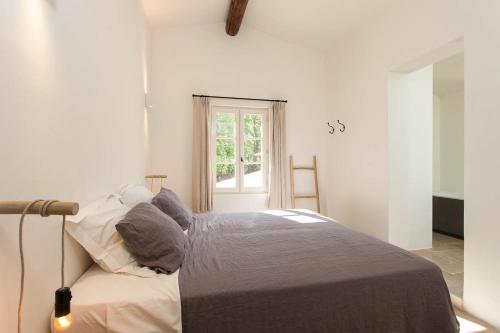 a white bedroom with a bed and a window at Les Amandiers in Bonnieux
