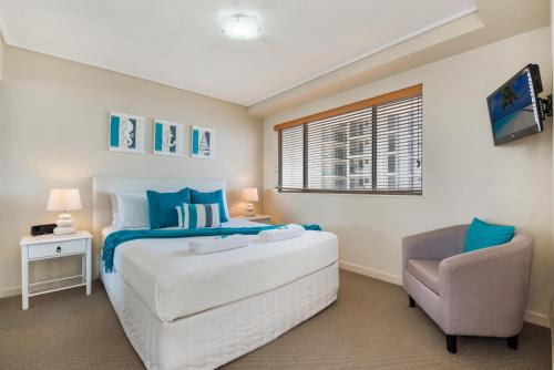 a hotel room with a bed, desk, chair and lamp at Seamark on First in Mooloolaba
