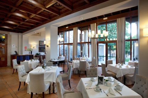 un restaurante con mesas y sillas blancas y ventanas en Parador de Caceres, en Cáceres