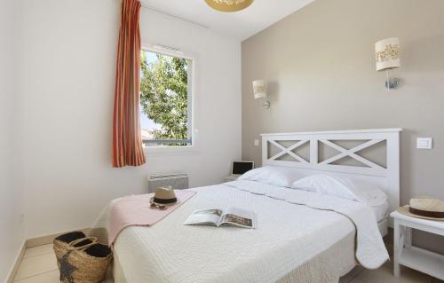 Un dormitorio blanco con una cama con un libro. en Résidence Odalys Le Mas des Flamants en Aigues-Mortes