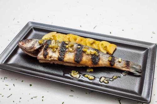 a grilled fish on a black plate with fruit at Hostal La Plaça in Erill la Vall