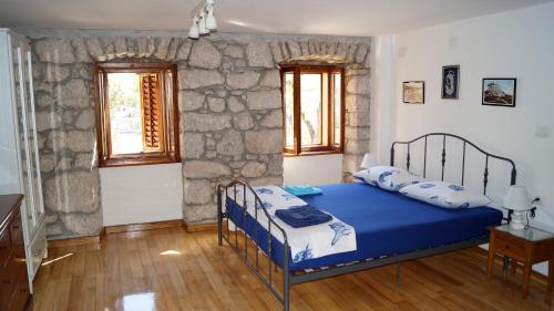 a bedroom with a blue bed and a stone wall at Apartmani Vila Angelina in Selce