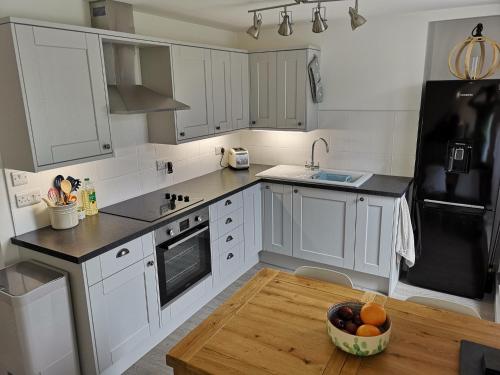 una cocina con armarios blancos y un bol de fruta en una mesa de madera. en Ty Isa en Nefyn