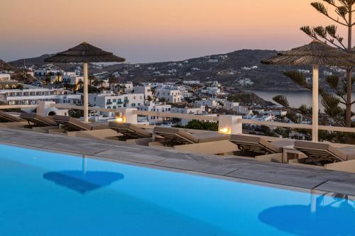 a pool with chairs and umbrellas and a city at Hotel Alkyon in Mýkonos City