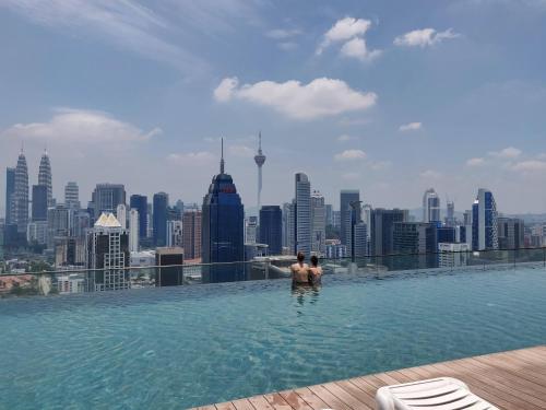 SkyBed Over The Sky Hostel @Regalia Suites & Residences KL في كوالالمبور: رجل يقف في مسبح لا متناهي على سطح مدينة