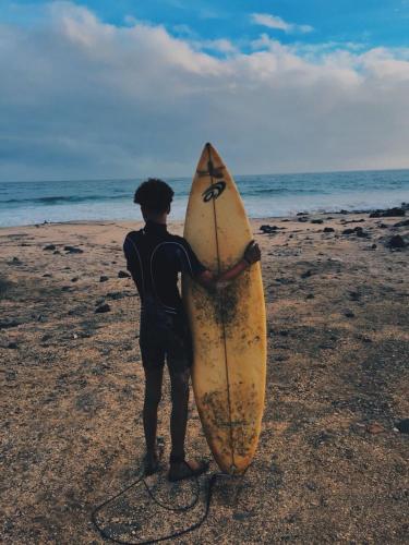 a man standing on the beach holding a surfboard at Casa Senador in Mindelo
