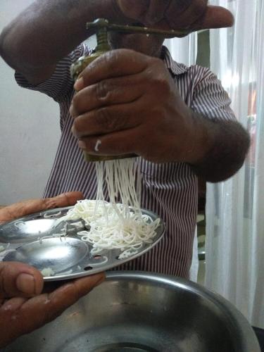 a man is adding noodles to a plate of food at Marari Bethsaida Homestay in Shertallai