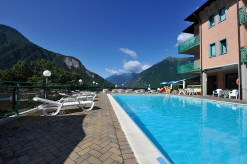 a swimming pool with chairs and a building and mountains at Hotel Torre in Sondalo