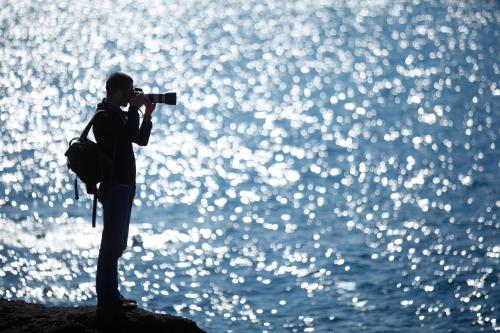 a man standing on a rock taking a picture of the water at Hotel Luci Del Faro in Calasetta