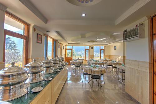 a dining room with tables and chairs and windows at Hotel Mountain face by Snow City Hotels in Manāli