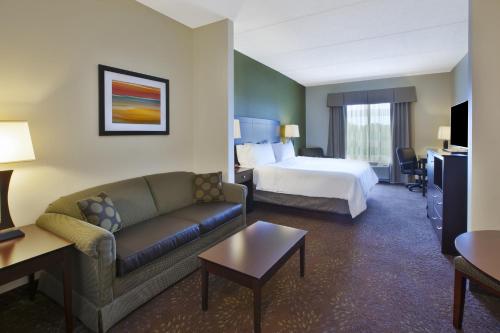 Holiday Inn Express & Suites Geneva Finger Lakes, an IHG Hotel في جنيف: غرفه فندقيه بسرير واريكه