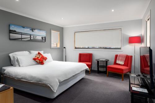 a bedroom with a bed and two red chairs at The Edgewater on Greville in Sanctuary Point
