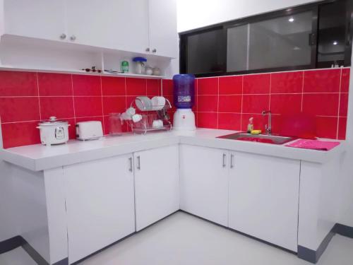 a kitchen with white cabinets and a red tile wall at Diodeth's Holiday Apartment in Butuan