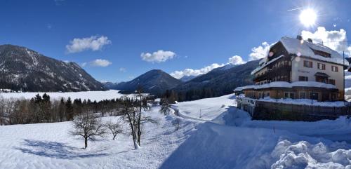 a building in the snow with mountains in the background at Hotel Nagglerhof am Weissensee in Weissensee
