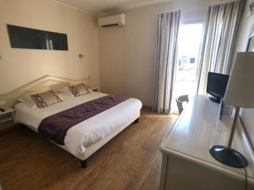a hotel room with a bed and a desk and a window at Hôtel Méditerranée in Le Lavandou