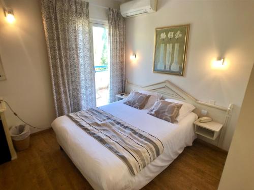 1 dormitorio con 1 cama blanca grande y ventana en Hôtel Méditerranée, en Le Lavandou