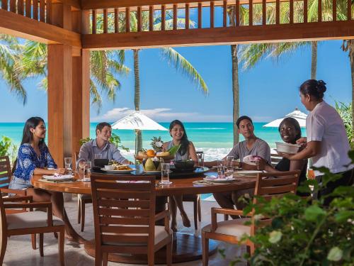 eine Gruppe von Menschen sitzt an einem Tisch am Strand in der Unterkunft Villa Nandana by Elite Havens in Natai Beach