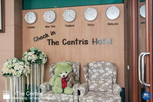 a teddy bear sitting in a chair with clocks on a wall at The Centris Hotel Phatthalung in Phatthalung