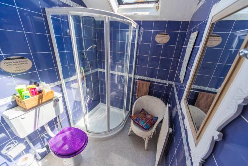 a blue tiled bathroom with a shower and a chair at Compton Guest House in Buxton
