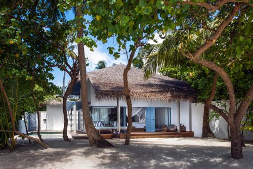 a house with a thatched roof on a beach with trees at Raffles Maldives Meradhoo in Gaafu Alifu Atoll