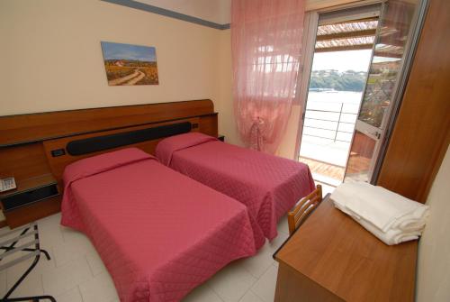 a bedroom with two beds with pink sheets and a window at Hotel Baia Del Sorriso in Castiglioncello