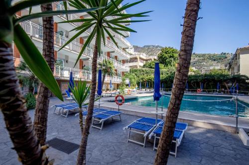 a resort with a pool with blue chairs and palm trees at Angelina Residence in Maiori