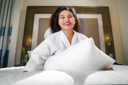 a woman sitting on a bed holding a pillow at Novotel Abu Dhabi Gate in Abu Dhabi