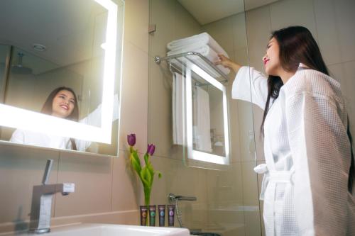 a woman standing in front of a mirror in a bathroom at Novotel Abu Dhabi Gate in Abu Dhabi