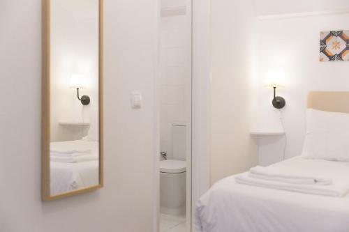 een witte kamer met een bed en een spiegel bij Casa Candeias in Évora