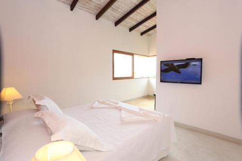 a white bedroom with a bed and a tv on a wall at Chalés Mariolinha in Ilhabela