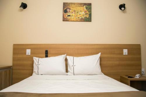 a bed with white pillows and a wooden headboard at Hotel Máximos in Itapetininga