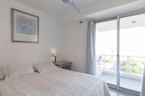 a white bedroom with a bed and a large window at Apartamento 24 in Punta del Este