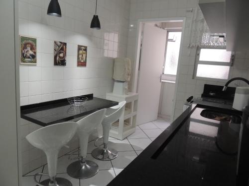 a kitchen with a black counter and white chairs at Apartamento Confortavel em Balneário Camboriu in Balneário Camboriú