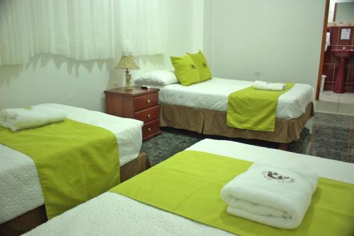 a room with three beds with green sheets and towels at Hostal Gosén in Puerto Baquerizo Moreno