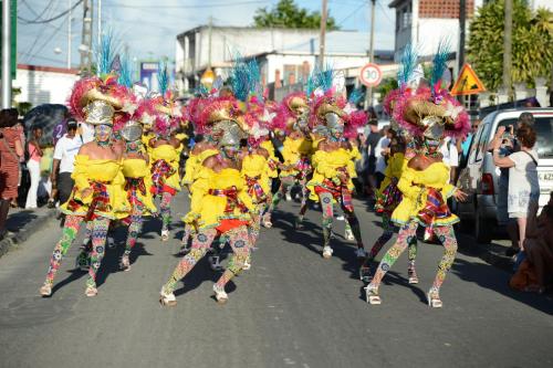 a group of people dancing in a parade on a street at studio "BLEU TURQUOISE" in Le Gosier