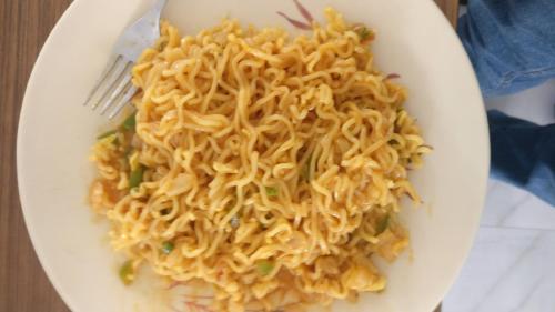 Un plato de fideos sobre una mesa con un tenedor. en Comfort Stay, en Faridabad