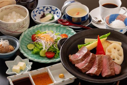 a table topped with plates of food with meat and vegetables at Tokushima Grandvrio Hotel in Tokushima
