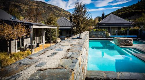 a swimming pool with a stone retaining wall next to a house at Cardrona Holiday Villa in Cardrona