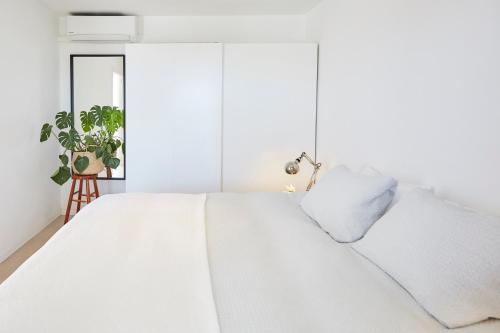 a white bedroom with a bed and a plant at Sunny Beachfront Escape in Castelldefels