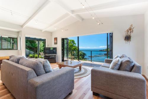 a living room with two couches and a view of the ocean at Beachfront Enclosure Bay - Waiheke Unlimited in Oneroa