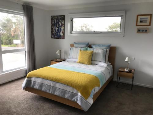 a bedroom with a bed with a yellow blanket and two windows at Snapper House in Phillip Island