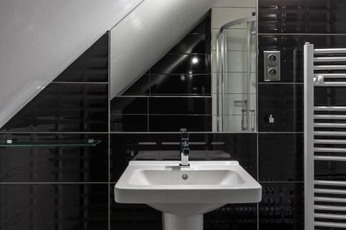 a white sink in a bathroom with black tiles at Hotel Grand in Čáslav