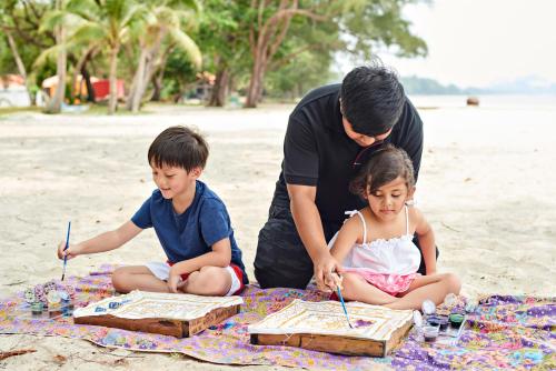a man and two children sitting on a blanket on the beach at Swiss-Garden Beach Resort, Kuantan in Kuantan